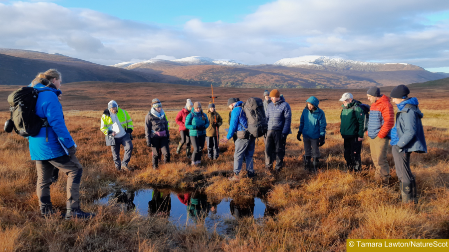 Group of people in outdoor clothing stood around a bog pool