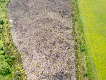 Aerial view of an oblong-shaped brown patch of land with green fields on one side.
