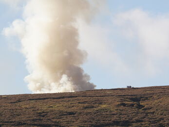 Plume of smoke rising from a moorland landscape.