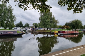 Canal boats are moored along a river with trees reflecting in the water