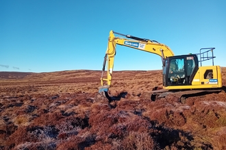 Yellow digger digging on brown peatland