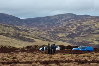 People and cars on a peatland with mountains behind