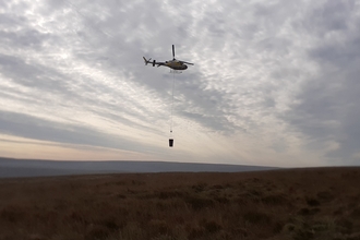 Helicopter flying over a remote peatland restoration site carrying a bucket with materials.