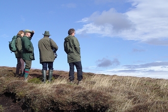 Four people in outdoor clothing looking out across a peatland landscape.