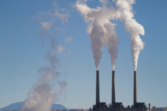 Three chimney stacks from a factory emitting smoke.
