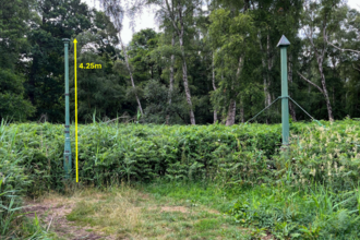 Two green metal posts sticking out of the ground in a woodland clearing. One is labelled as being 4.25m above the surface.