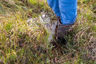 A child's feet in a pair of wellies, stood in a small peatland pool.