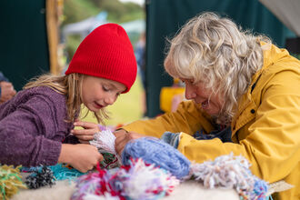 A young child and older woman peering at balls of wool on a piece of fleece