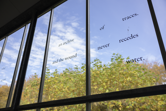 Scattered words on a glasshouse window. Outside the window is a blue sky with fluffy white clouds and trees in early autumn colours of pale green, yellow and orange.