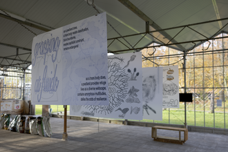Four large canvases suspended in a metal strcuture with glass walls. The canvases feature various drawings and text that says 'grasping of fluids'.