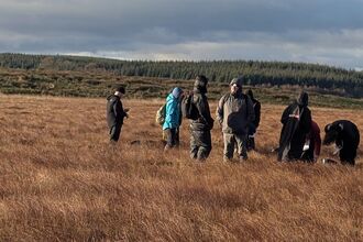 A group of young people in outdoor clothing stood in long grass.