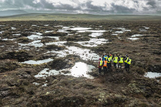 Aerial view of a group of people in high-vis jackets on a peatland landscape with lots of bog pools.