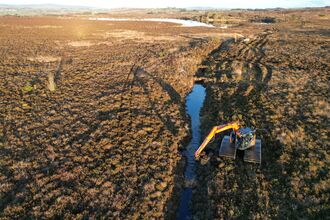 Aerial view of a digger next to a channel of water running across a bog landscape.