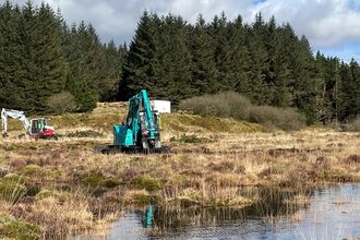 Two diggers on a peatland restoration site with large bog pools, and plantation forestry in the background.