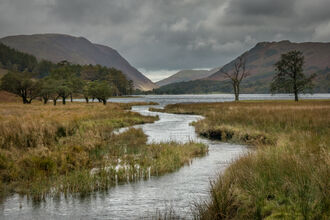 View of waterway winding into a lake with mountains in the background.
