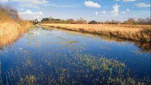 Lowland waterway with windmill and some buildings on the right side of the embankment