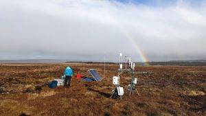 Scientific equipment set up on a peat bog next to a scientist in waterproof clothing. Credit Mhairi Coyle