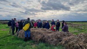 People grouped together, standing and sitting on a baled crop.