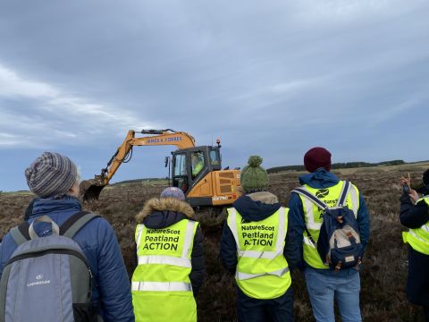 Group looking at the digger demonstrating the peat damming technique