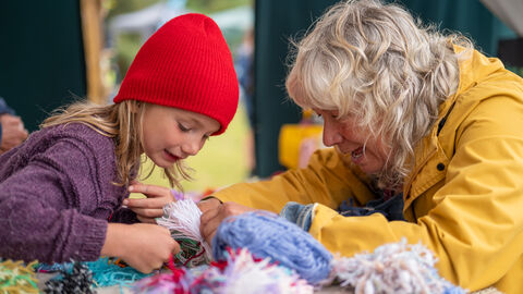 A young child and older woman peering at balls of wool on a piece of fleece