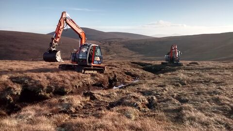 Two diggers on a drained peatland next to a gully. There is blue sky and a mountain in the distance.