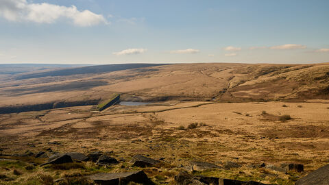 Peatland landscape with rolling hills and clouds dotted across a blue sky.