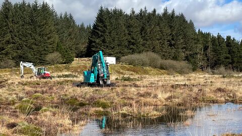Two diggers on a peatland restoration site with large bog pools, and plantation forestry in the background.
