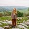 Person stood on rocks in a grassy area with hills and trees in the background.