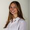 Poppy McClennon in a white shirt smiling at the camera in front of a plain background.