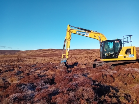 Yellow digger digging on brown peatland
