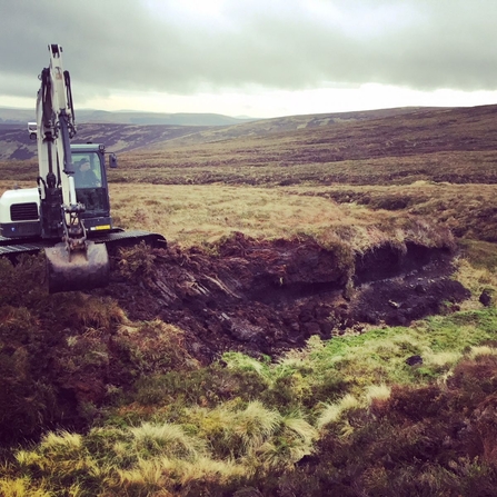Machine operator reprofiling a bare peat hag.
