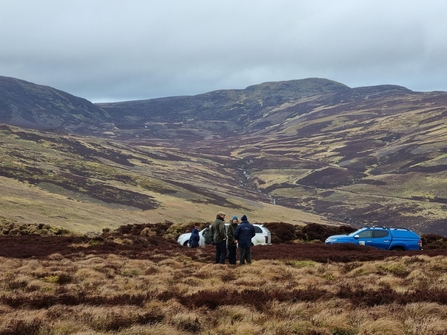 People and cars on a peatland with mountains behind