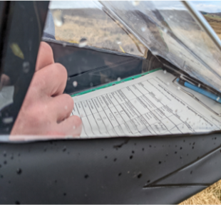 Close up of a waterproof clipboard and a hand writing notes on a survey form.