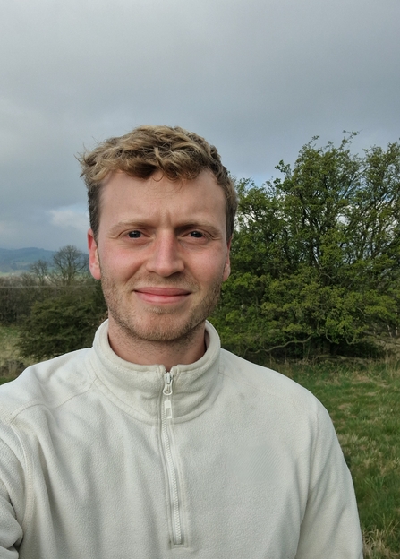 Person wearing a white top with trees and vegetation in the background