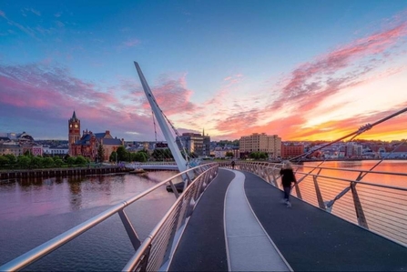 Bridge of a calm river looking towards a city skyline with sunset on the water