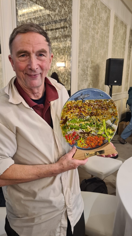 Richard Lindsay holding a glass sculpture depicting a peatland scene