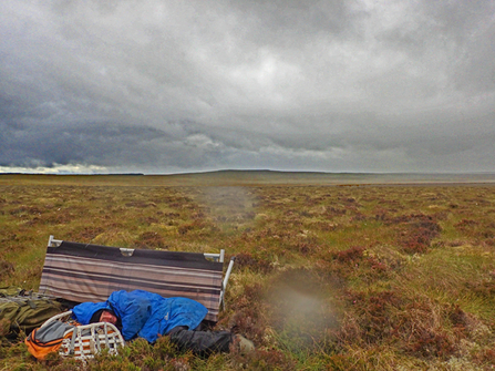 Blanket bog landscape with a figure in waterproof clothing curled up on the ground