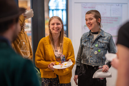 Two young people smiling and holding paper plates.