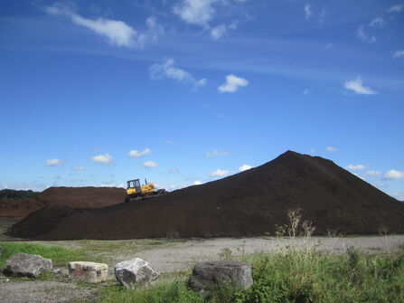 Large pile of extracted peat with a tracked vehicle driving up it.
