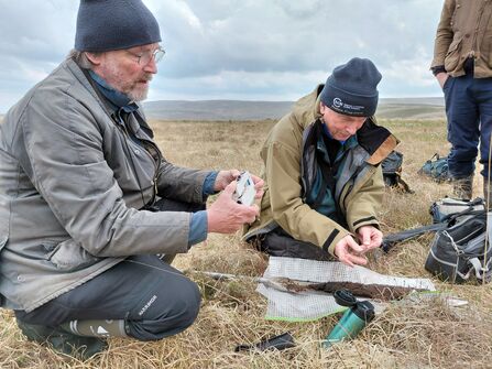 Peter Jones and Richard Lindsay kneeling on a grassy peatland looking at equipment.
