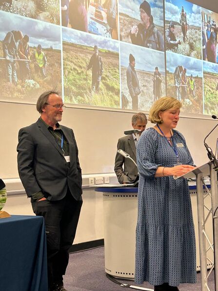 Mannon Lewis stood at a lectern with Peter Jones behind her as she reads his nomination.