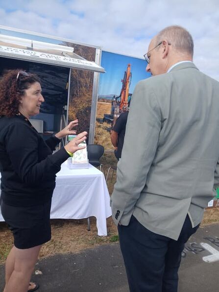 Two people in discussion in front of a pop-up banner featuring a photograph of a digger.