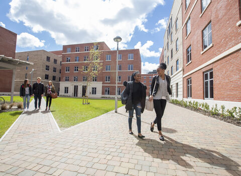 Two groups of people walking along a paved path between red brick buildings.