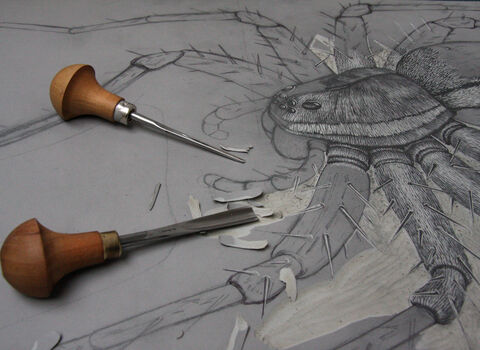 Close up of a part-completed linocut of a spider with the cutting tools lying on the lino.
