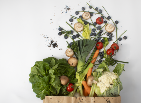 Scattered paper bag of lettuce, leeks, celery, carrots, mushrooms, blueberries and tomatoes.